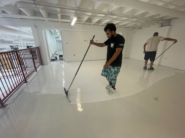 Two people cleaning a glossy white floor in a bright indoor space
