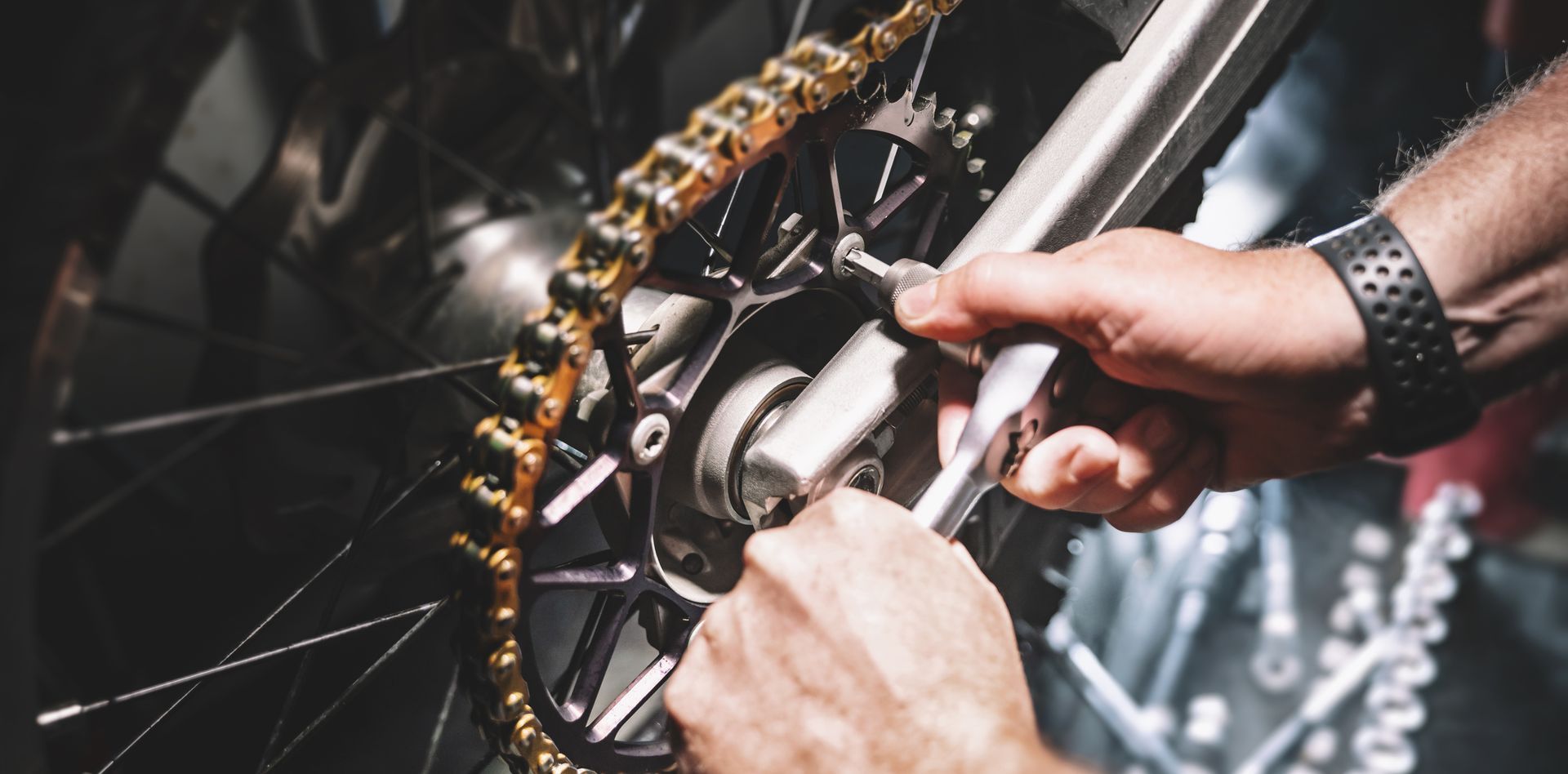 Un hombre está arreglando la cadena de una motocicleta con una llave.