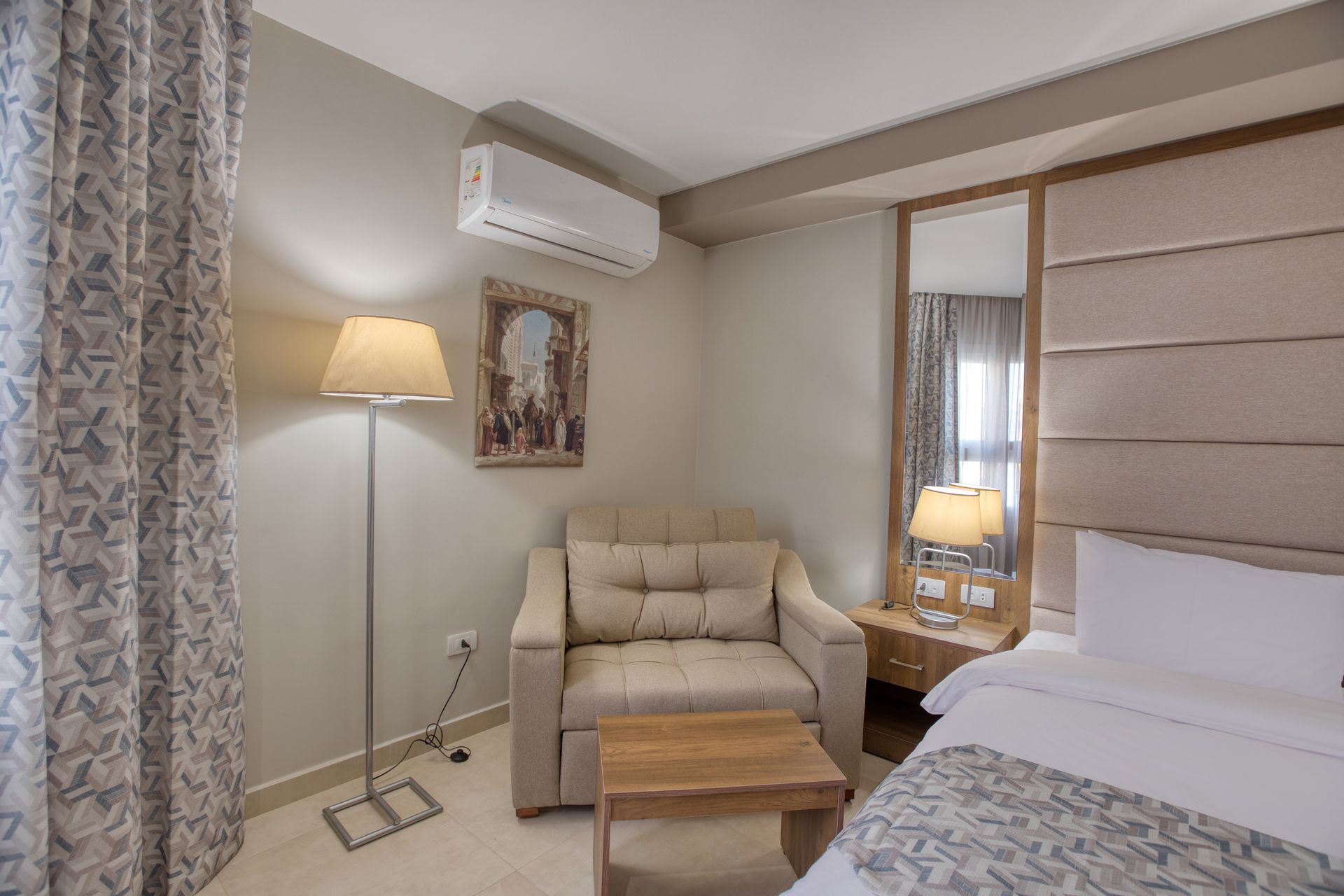 A hotel room with a bed , chair , table and mirror.