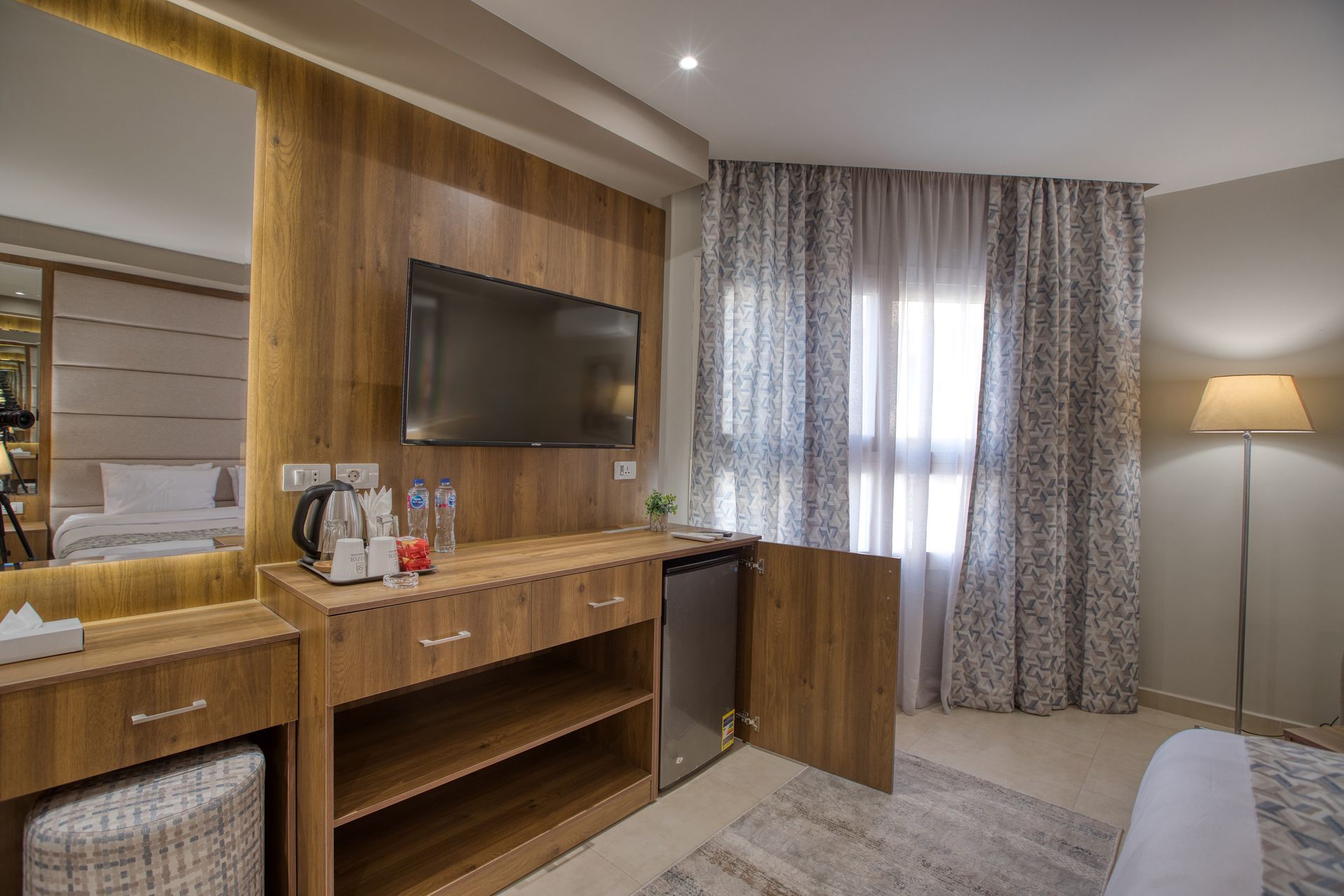 A hotel room with a bed , television , dresser and mirror.
