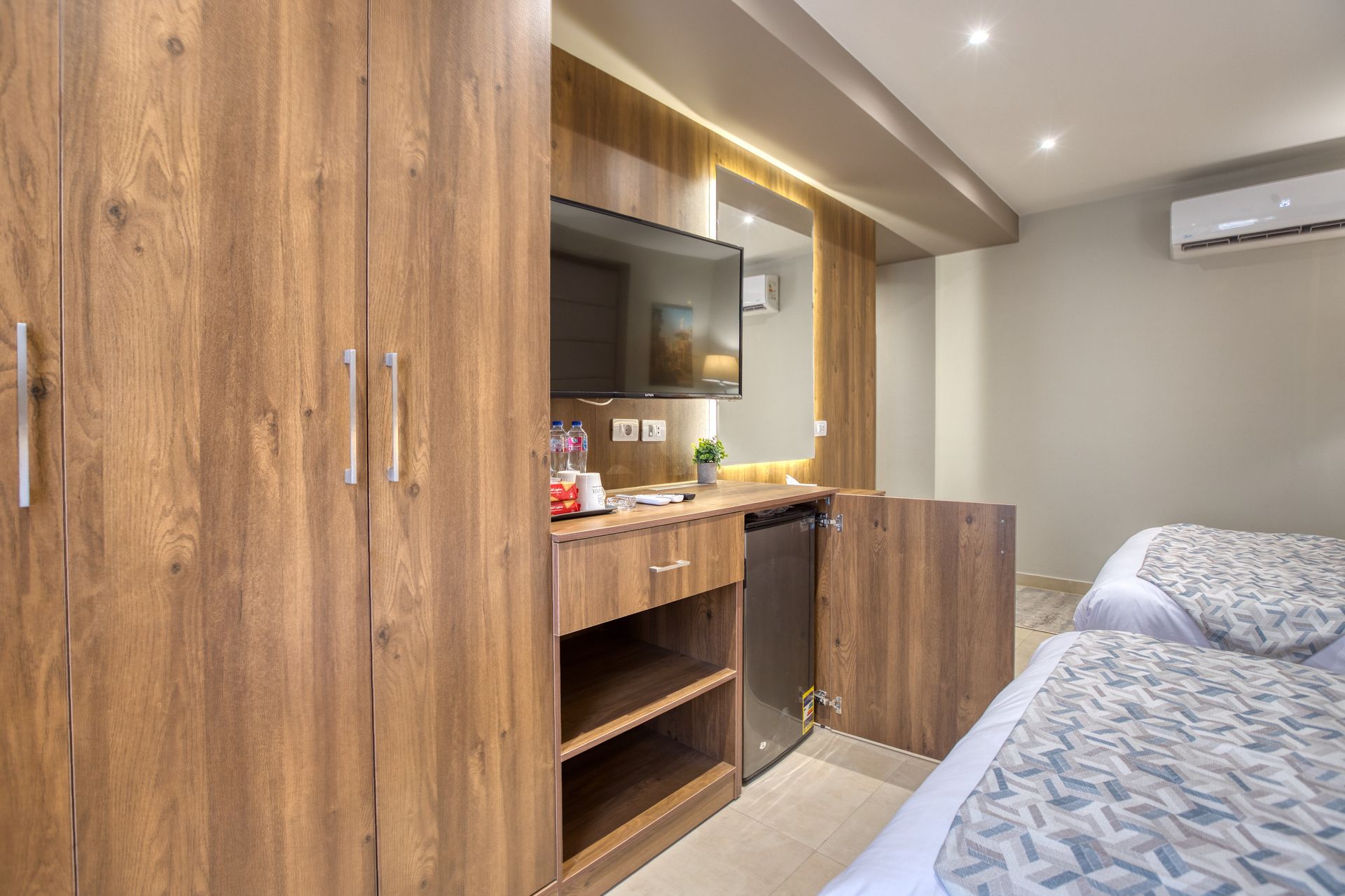 A hotel room with two beds , a desk , a television and a refrigerator.