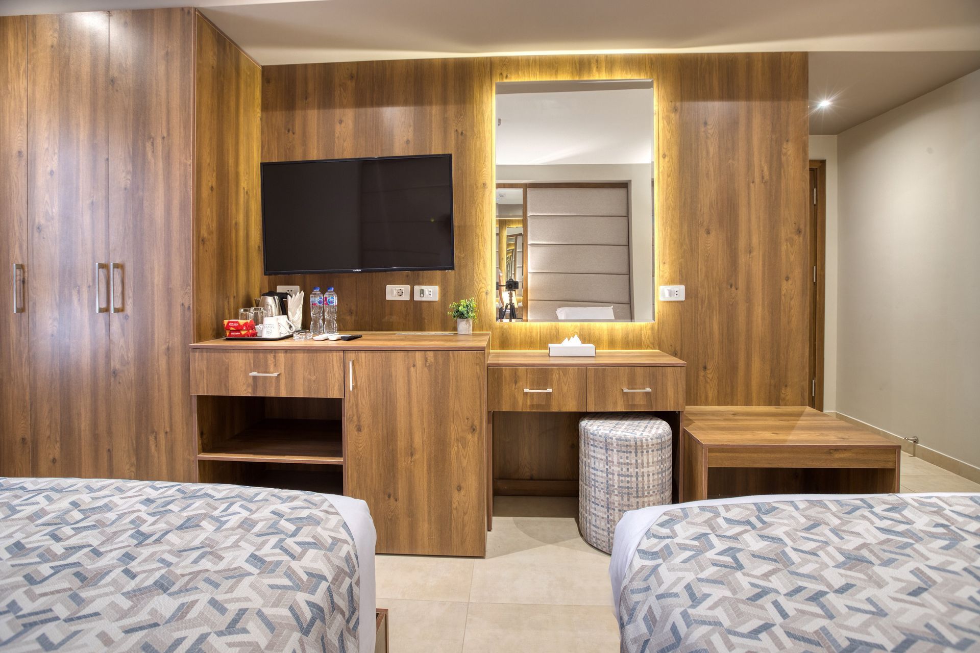 A hotel room with two beds , a desk , a television and a mirror.