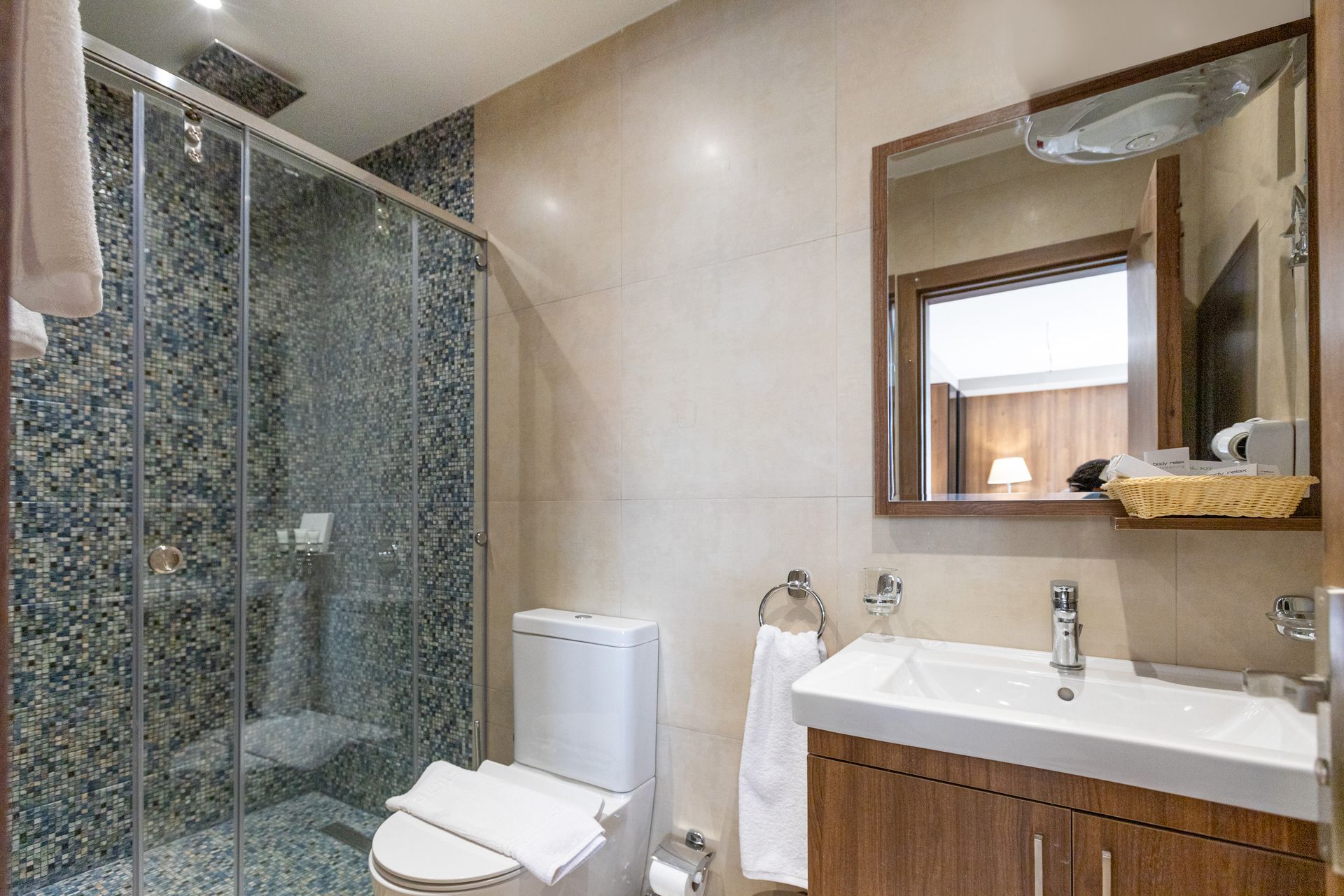 A bathroom with a toilet , sink , mirror and shower.