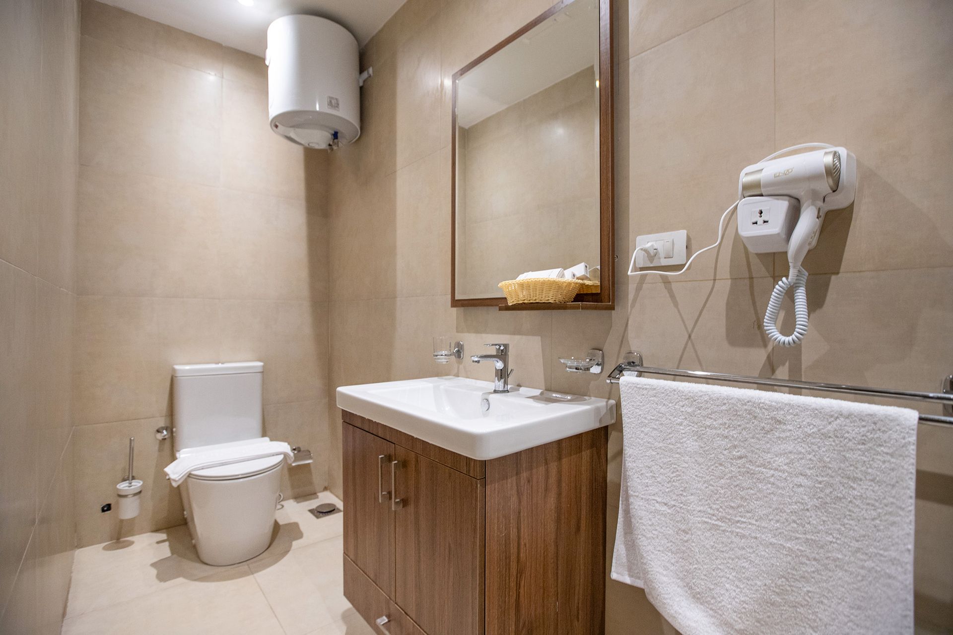 A bathroom with a toilet , sink , mirror and hair dryer.