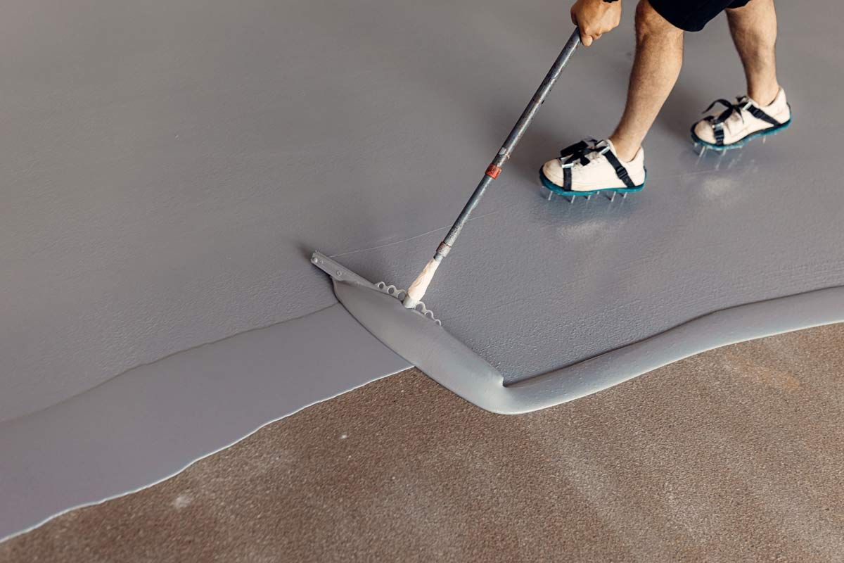 A Person Applying Epoxy Coating — Petone, Waikato — Industrial Floor Care A person is painting a concrete floor with a roller.