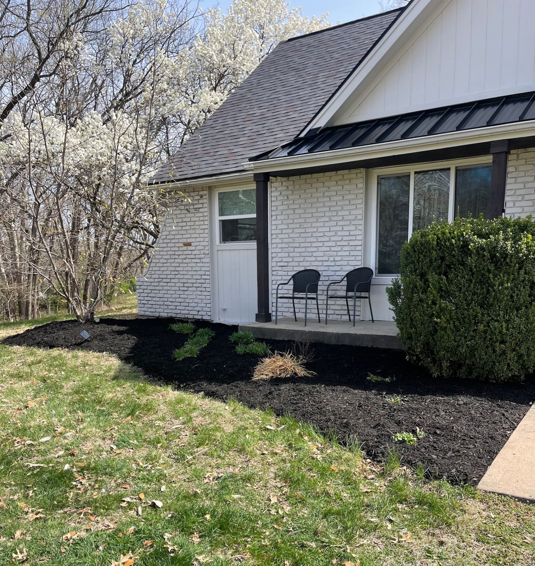 House exterior with white brick, black roof, and manicured landscaping.
