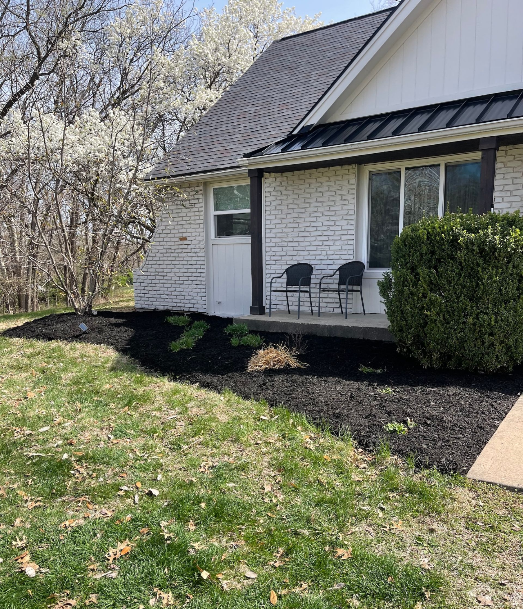 Curb appeal: a house with white brick, black roof and trim. Fresh black mulch in the flowerbeds and chairs on the porch.