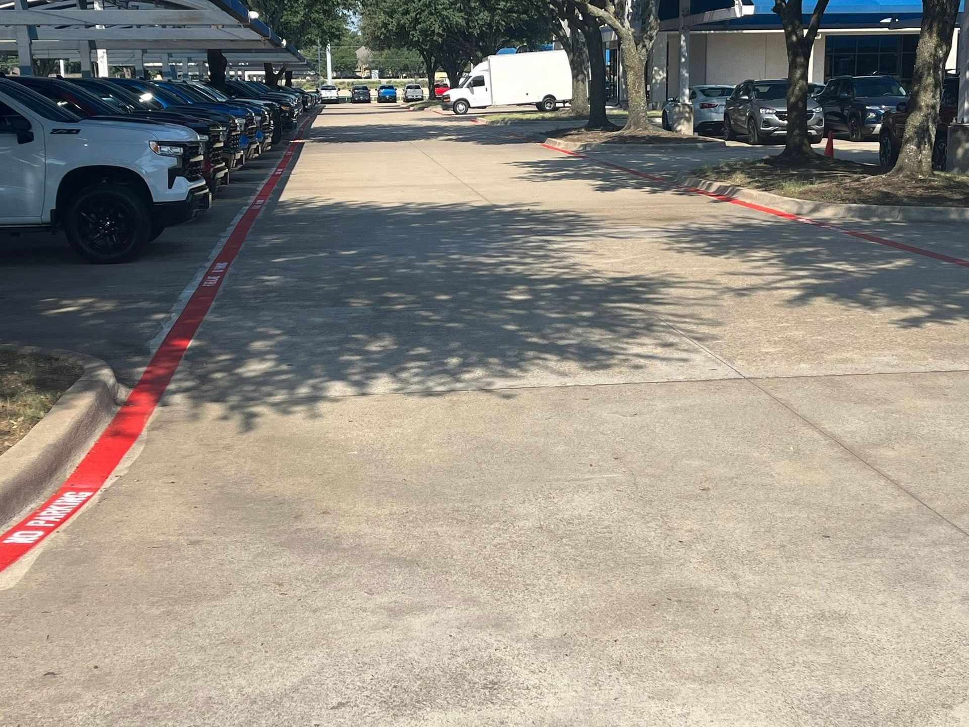 Parking lot with rows of cars, red curb markings, and shaded concrete.
