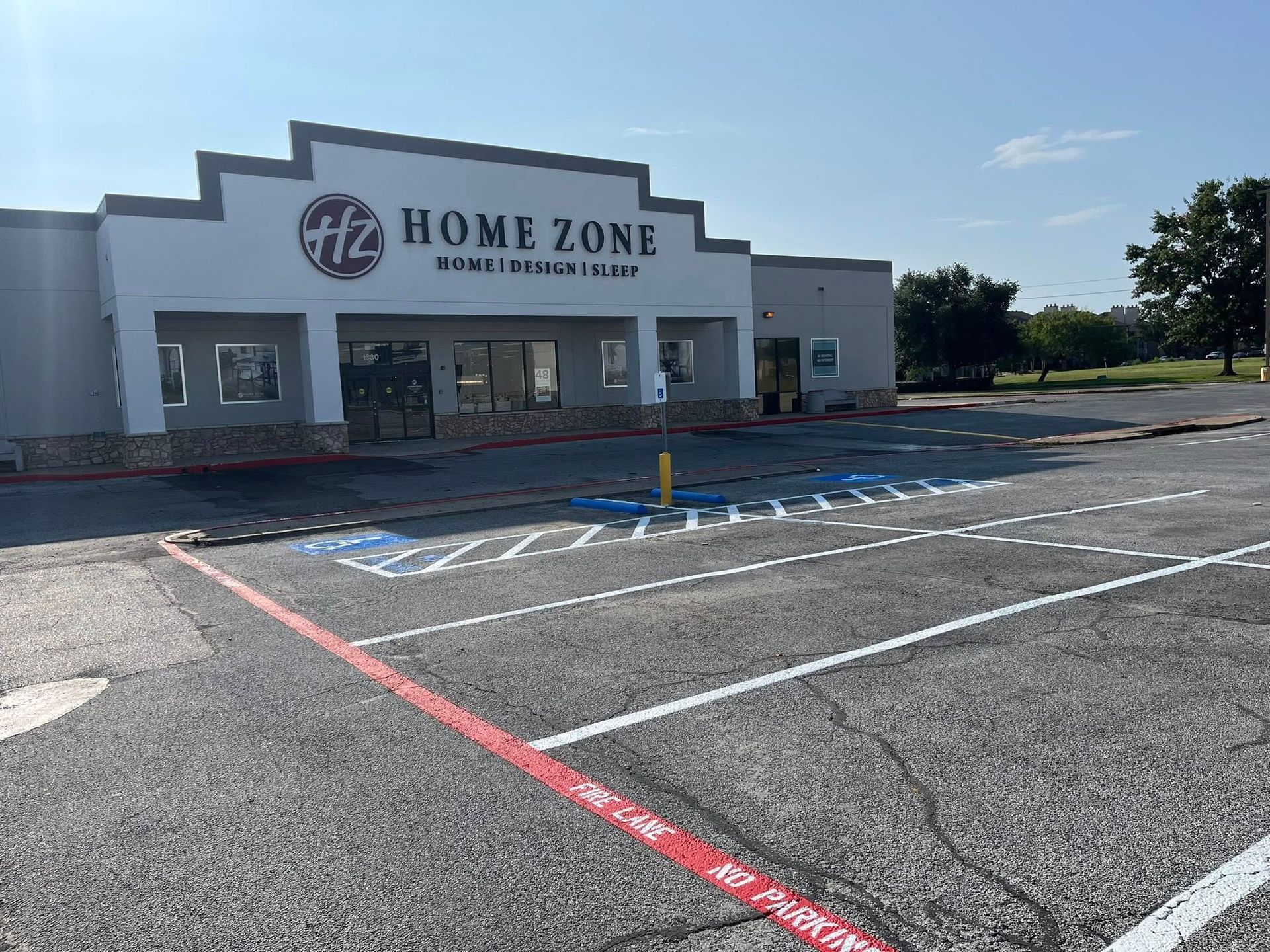 Home Zone store with empty parking lot and marked accessible parking spaces. Blue sky.