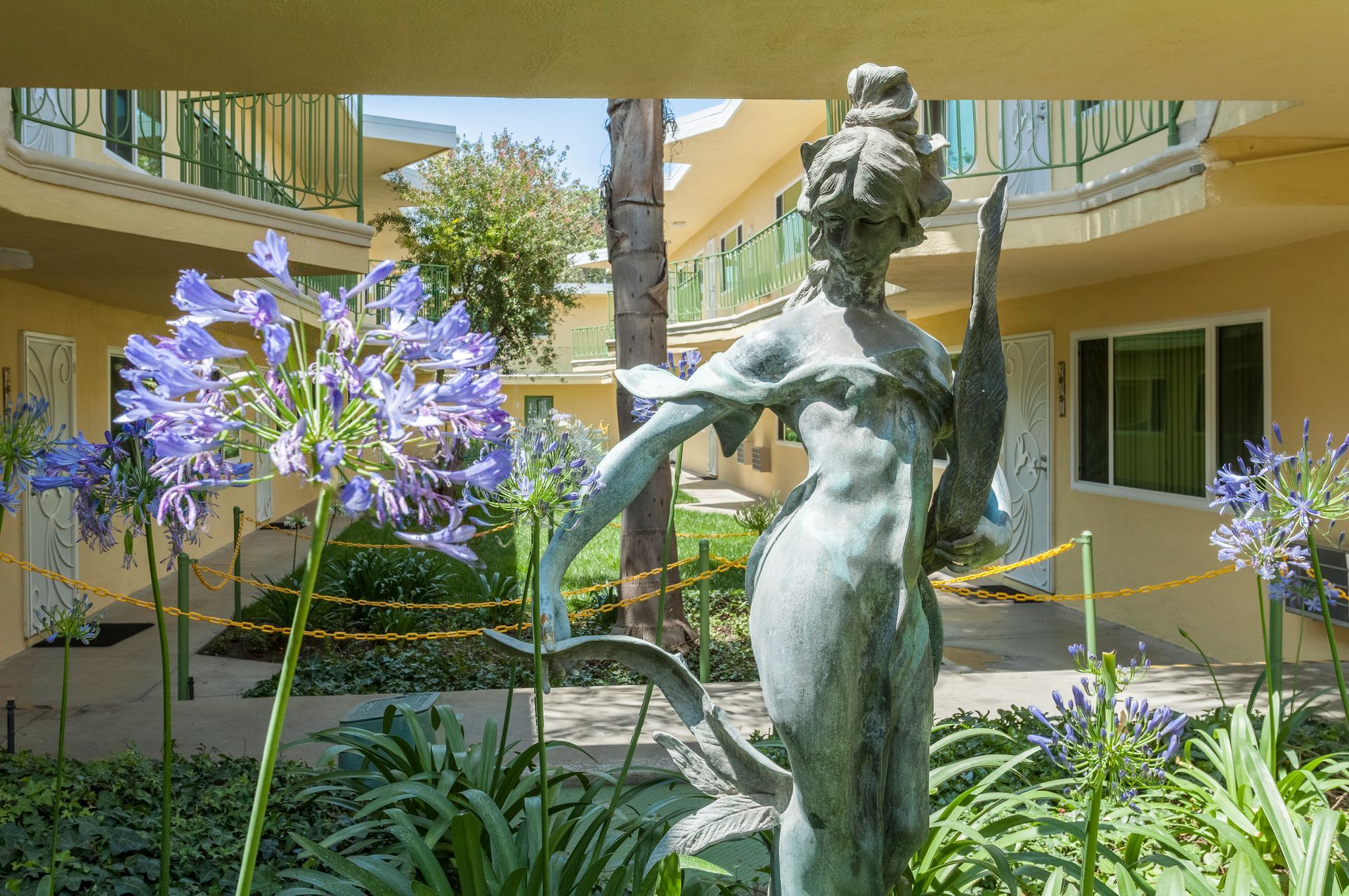 A statue of a woman holding a swan in a garden in front of a building.
