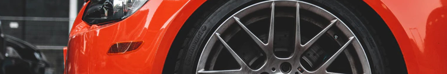 Close-up of a red sports car’s front wheel and fender with a black alloy rim and tire | 106th Street Tire & Wheel