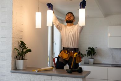 A man is installing a light fixture in a kitchen.