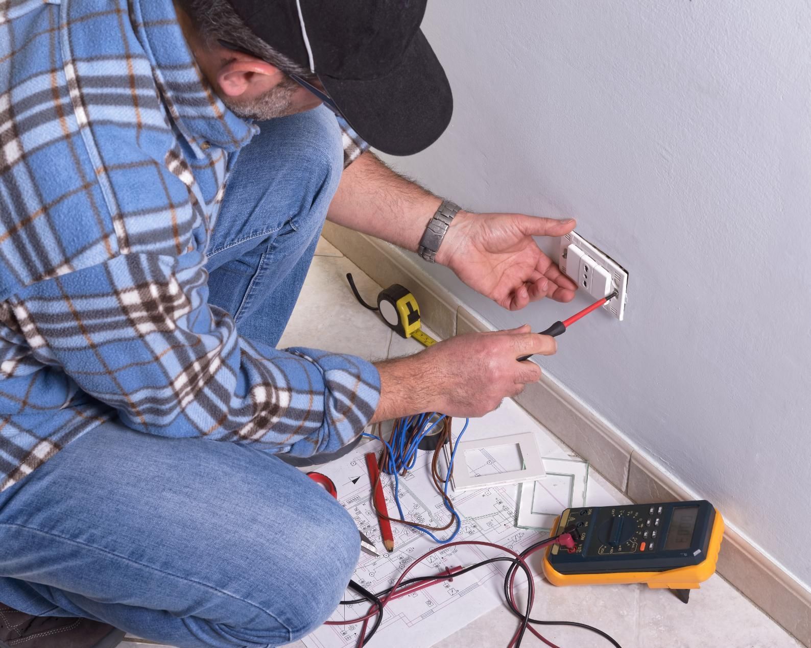 A man is kneeling on the floor working on an electrical outlet.
