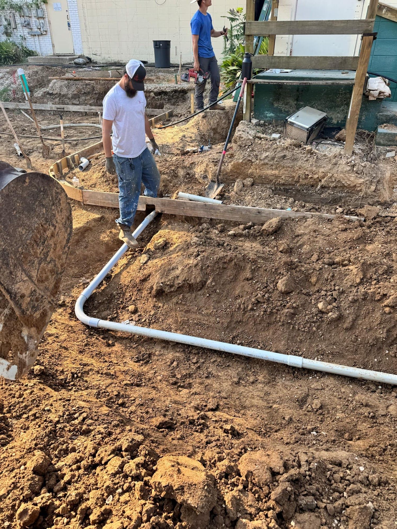 Two workers install PVC pipes in a dirt trench outdoors.