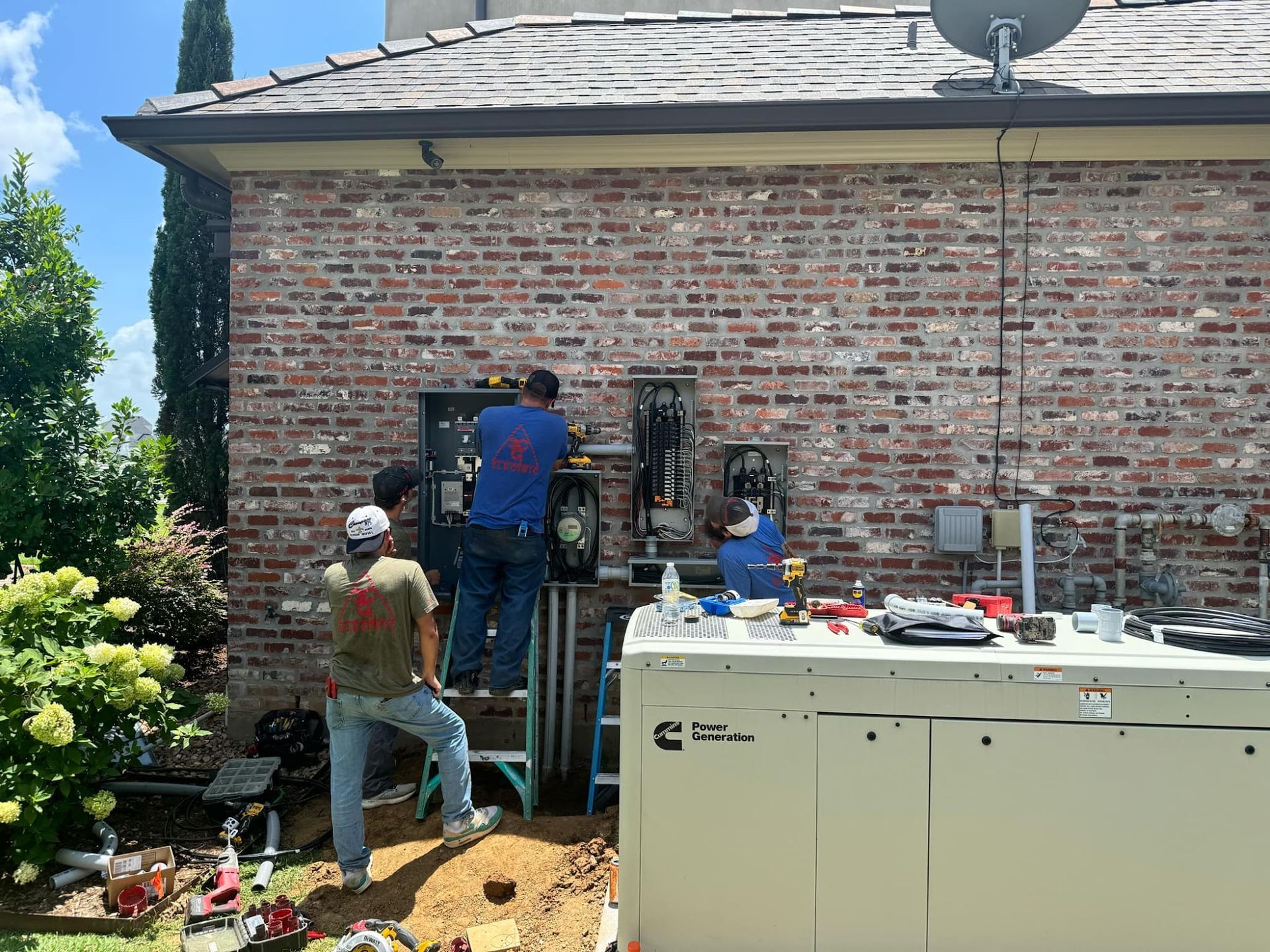 Three workers installing electrical equipment on a brick wall, near a generator. Tools and parts are scattered.