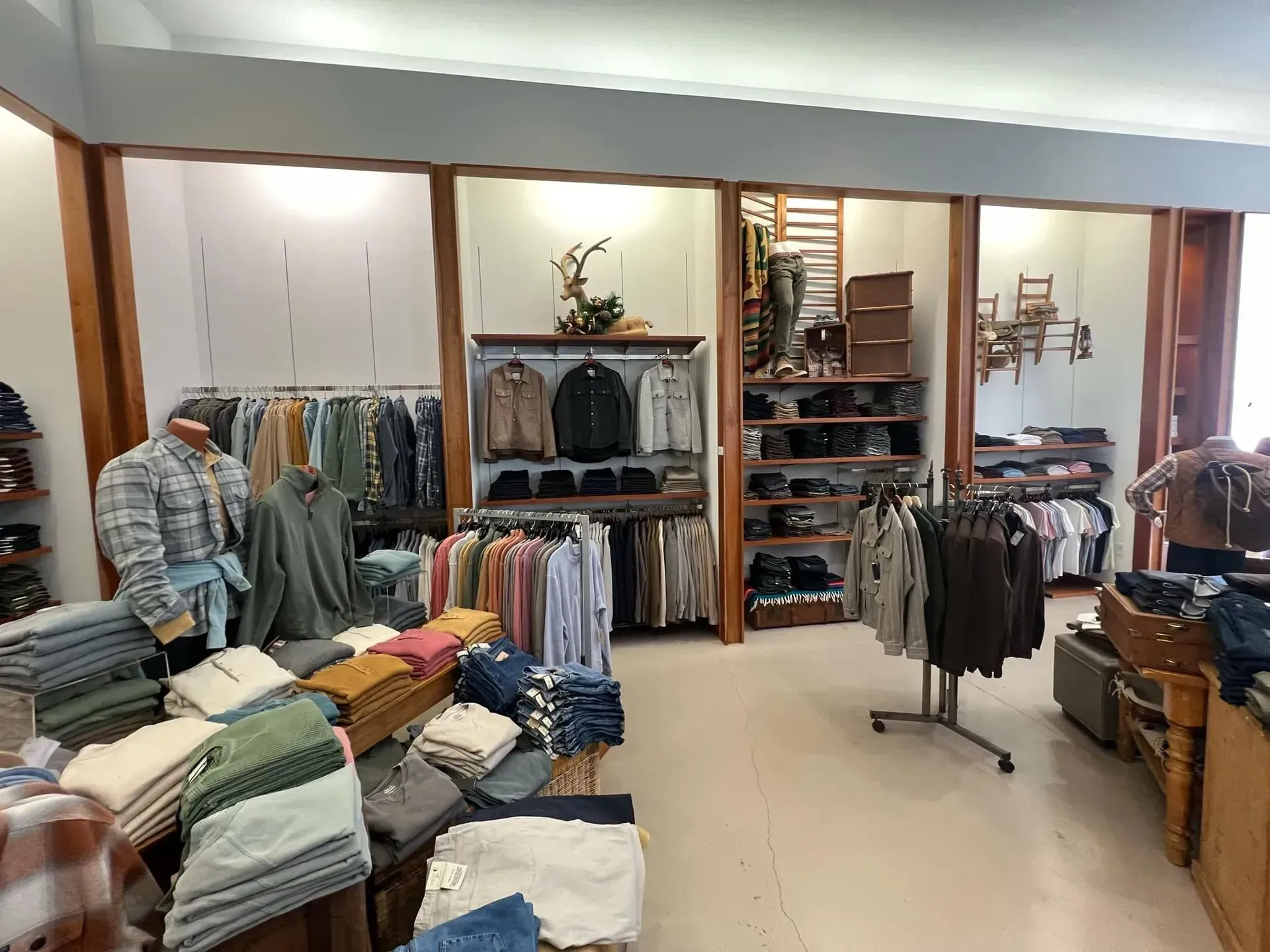 Clothing store interior with racks of shirts, pants, and sweaters. Displayed on shelves and a mannequin.
