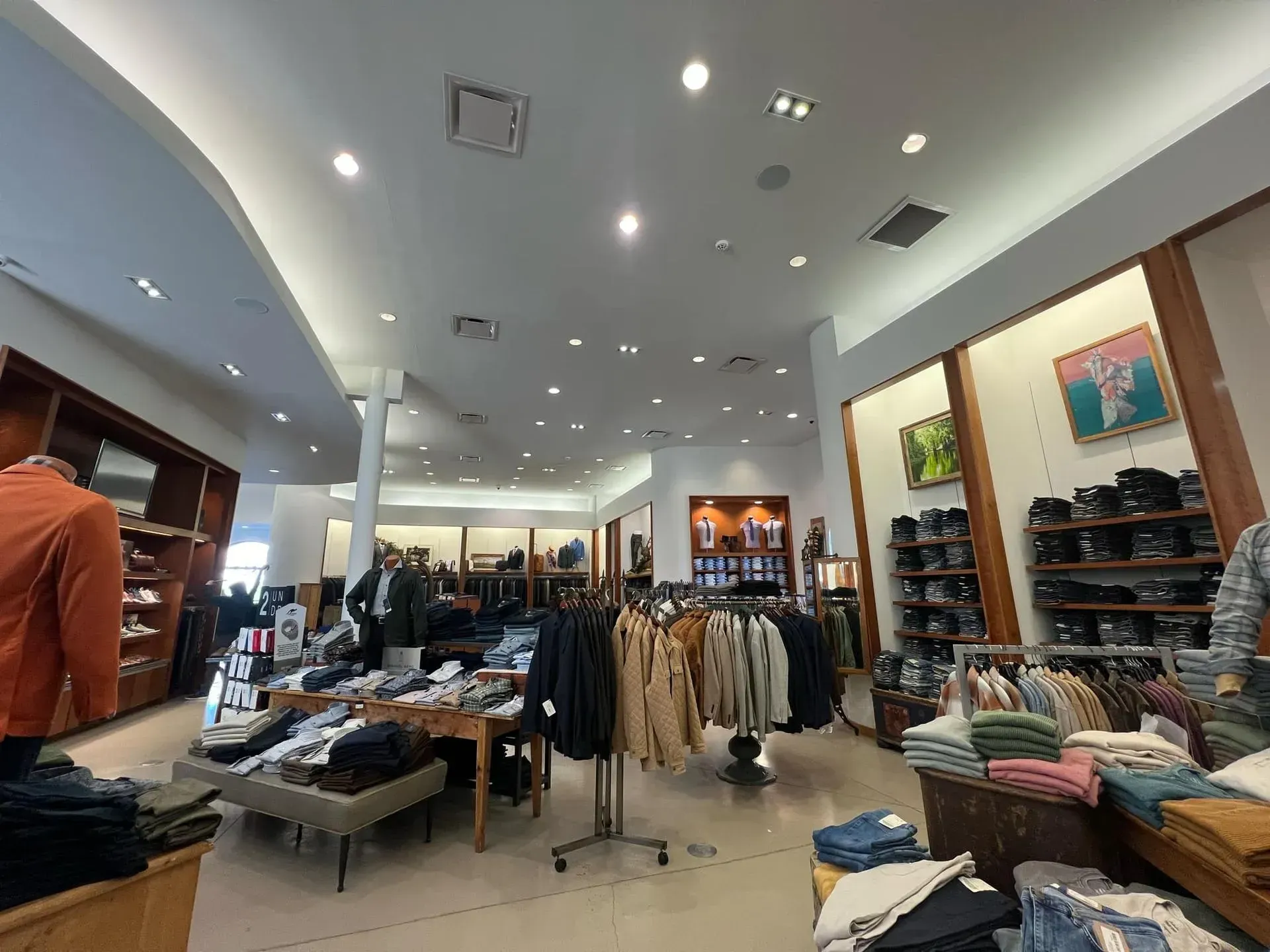 Inside of a clothing store, displaying various garments, with customers browsing.