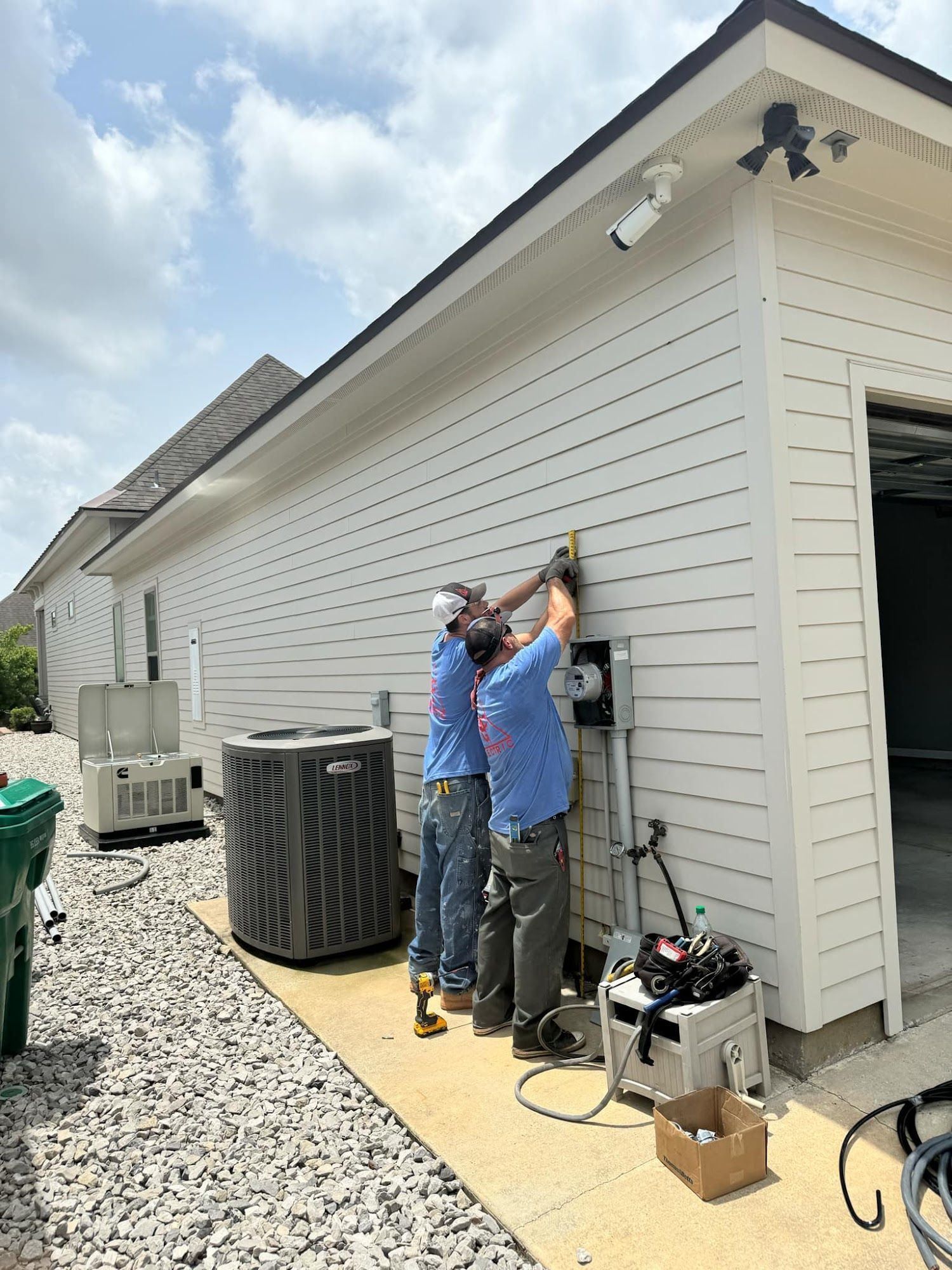 Two workers installing electrical equipment on a white house exterior near an AC unit.