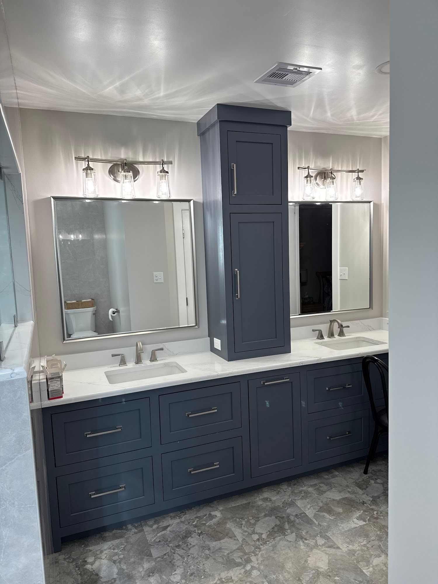 Bathroom with navy blue vanity, mirrors, and tall cabinet.