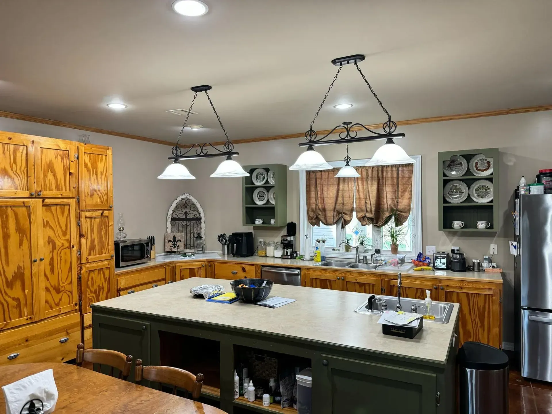 Kitchen with wood cabinets, green island, hanging lights, and stainless steel appliances.