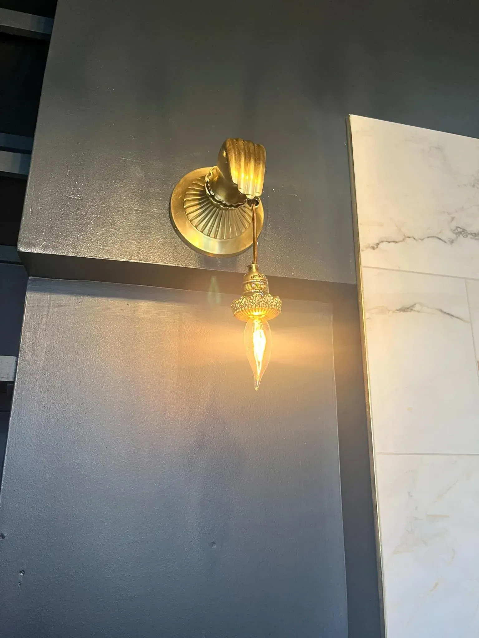 Gold sconce with a decorative fixture emitting warm light on a dark wall.