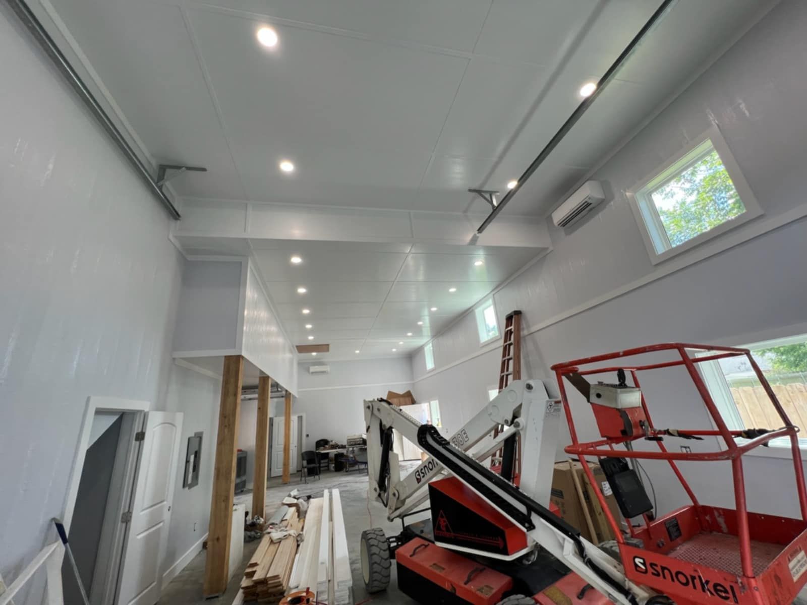 Interior construction site: white walls and ceiling, machinery, recessed lights, partially finished.