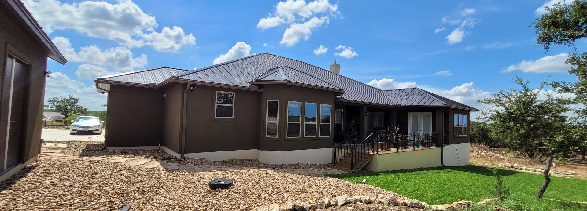 Brown house under construction with exposed roof framing, gravel yard, and blue sky with clouds