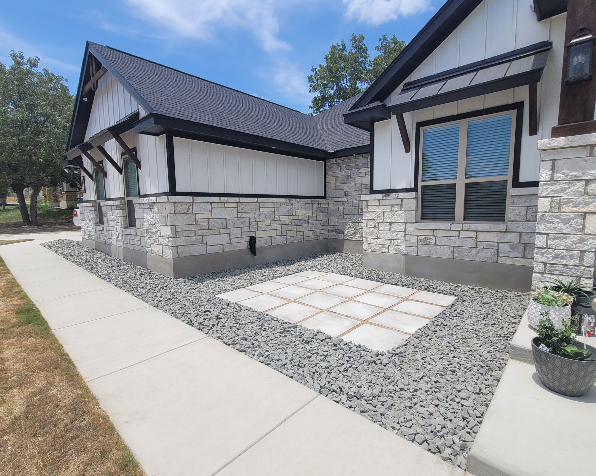 Modern stone house exterior with dark roof, large windows, and a gravel and paver front walkway