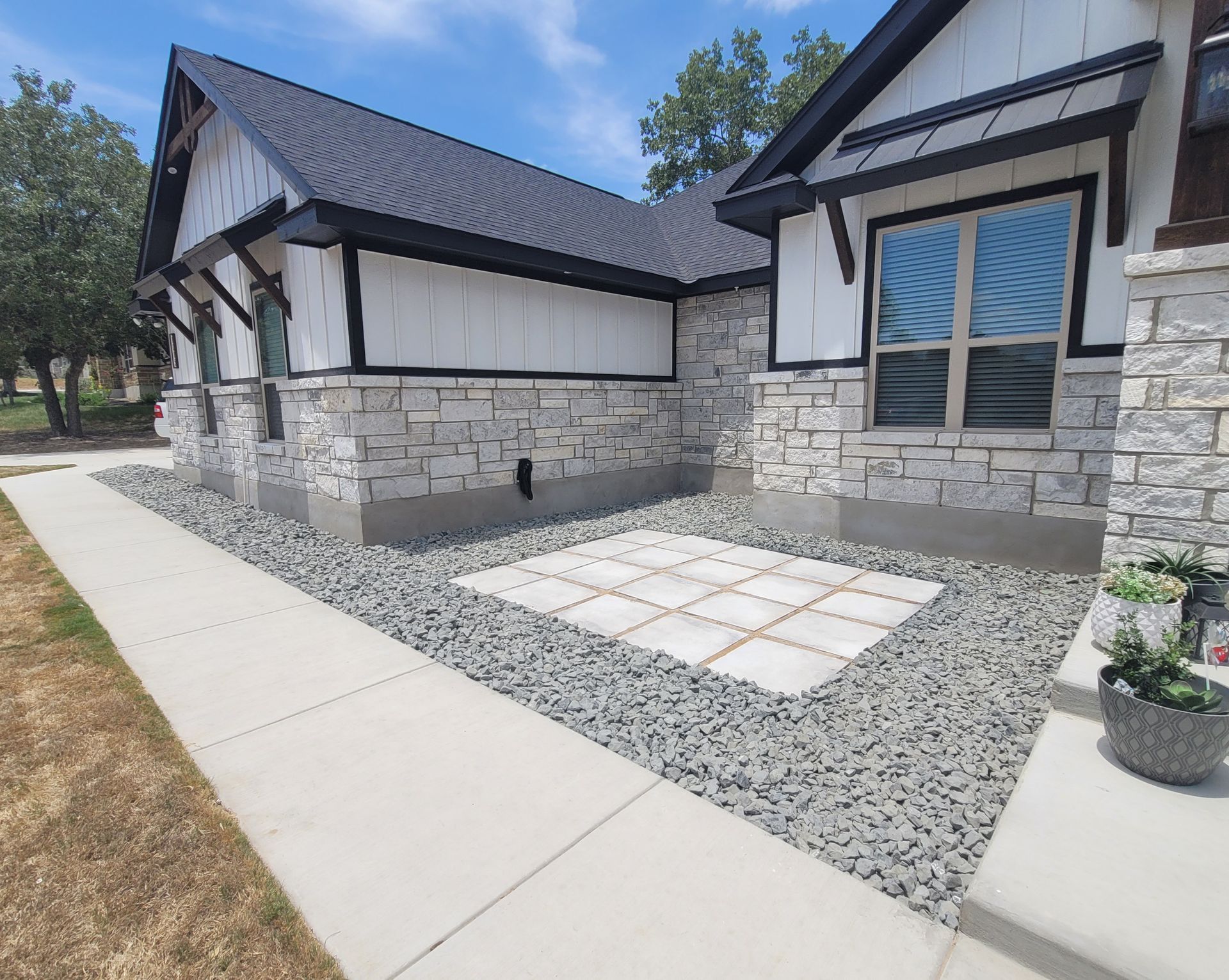 Modern stone-and-white house exterior with a concrete walkway and gravel landscaping under a blue sky