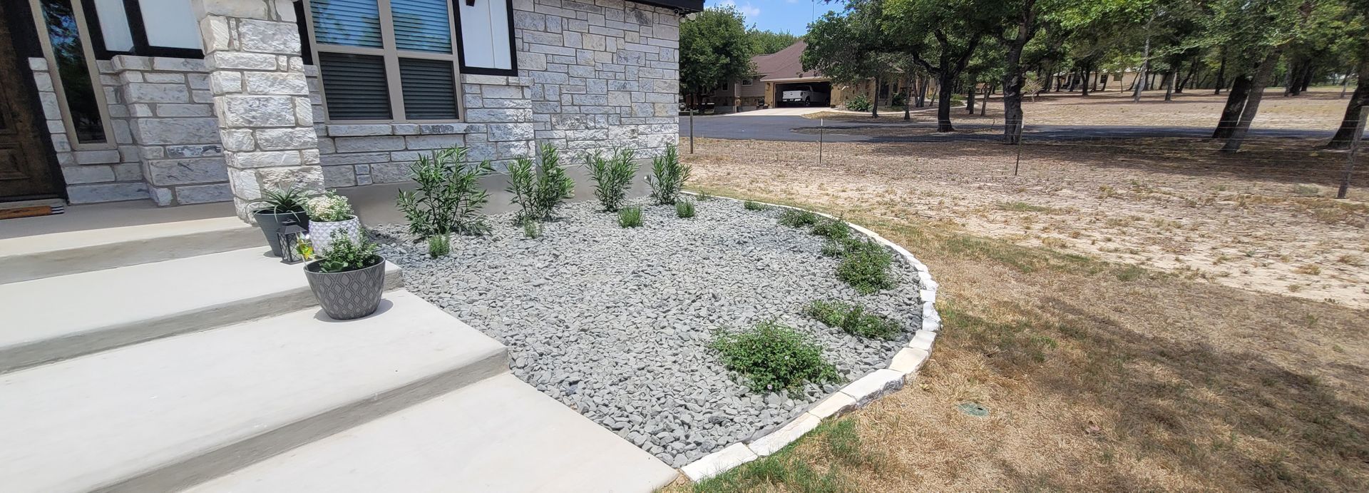 Front porch with steps, potted flowers, and a curved rock garden beside a house.