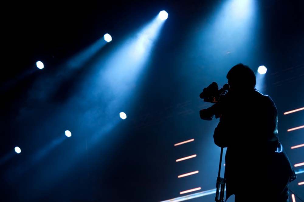 Silhouetted singer onstage under blue spotlights, holding a microphone during a live performance