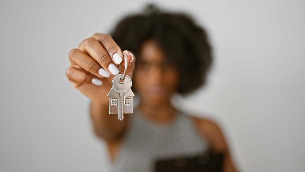 Hand holding a house key toward the camera, with a blurred person in the background