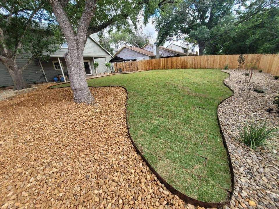 Backyard lawn with mulch beds, a large tree, and a wooden fence in the background