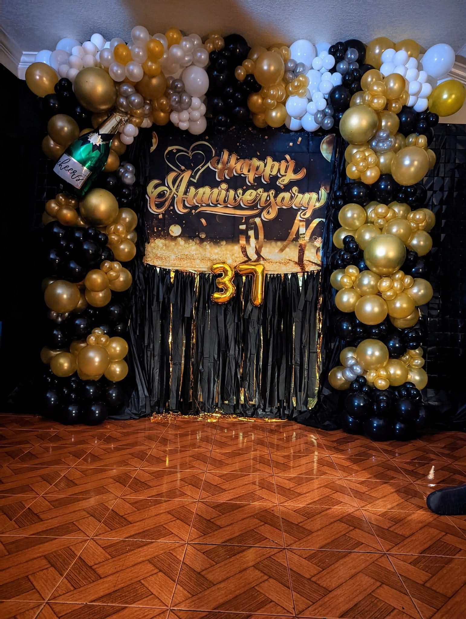 Black, gold, and white birthday balloon backdrop with gold “Happy Birthday” sign and number 31 on a parquet floor