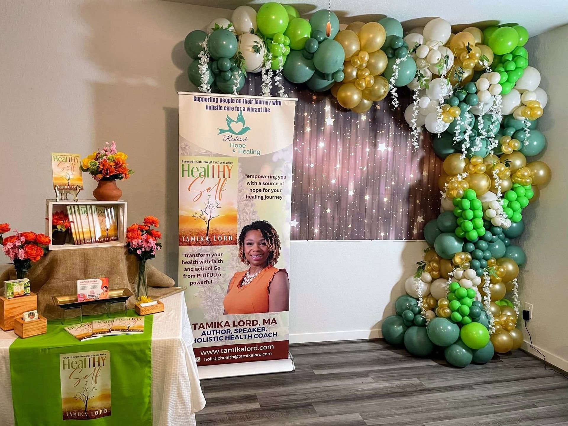 Party display with green and gold balloons, a banner, and a decorated table in a small room