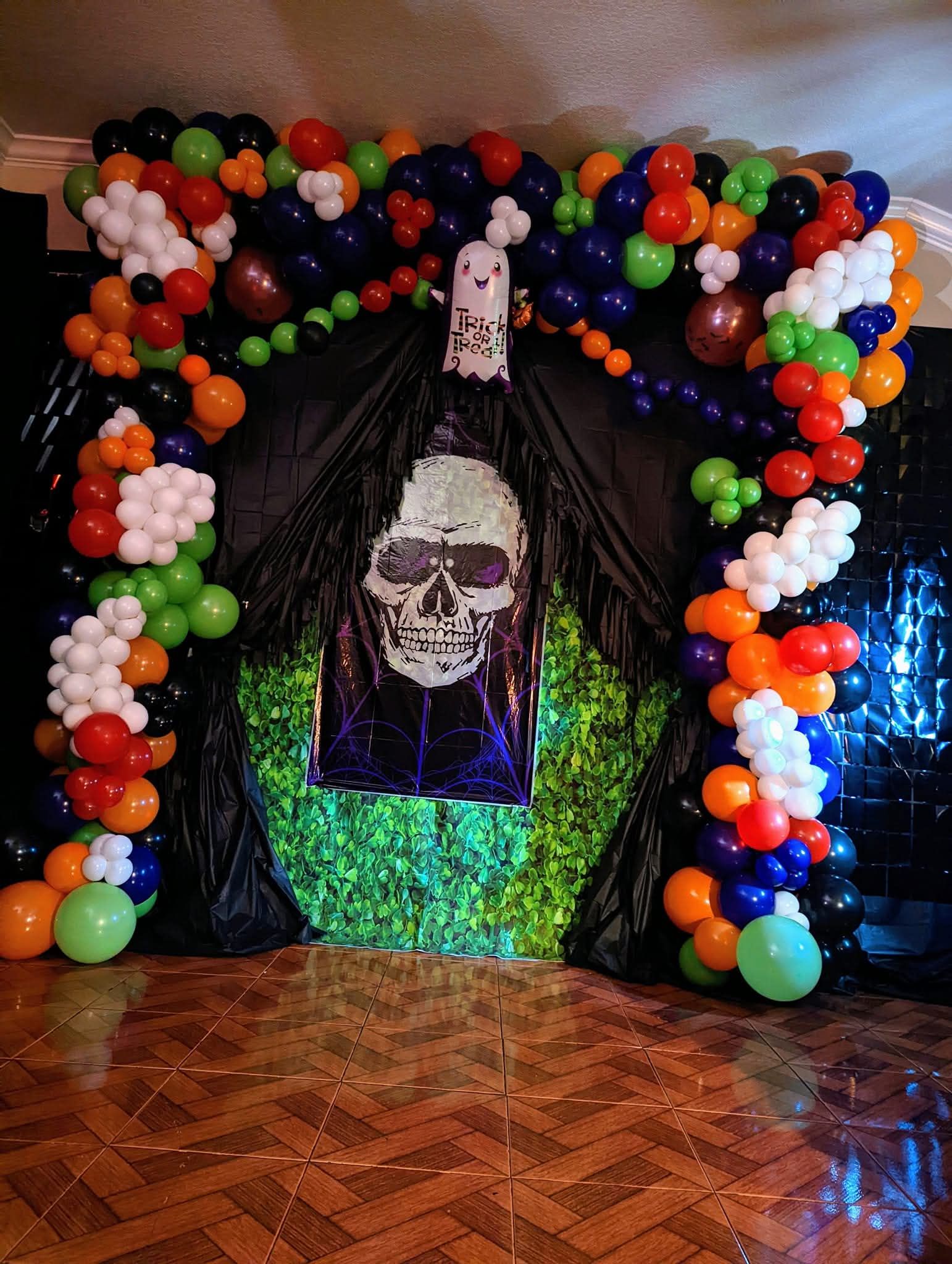 Balloon arch framing a black curtain backdrop with a smiling face portrait and green tinsel on a wooden floor