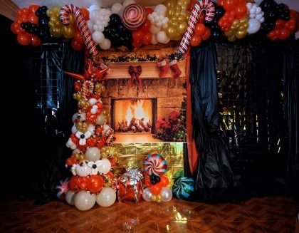Festive balloon arch around a lit fireplace with black drapes and colorful balloon clusters on the floor