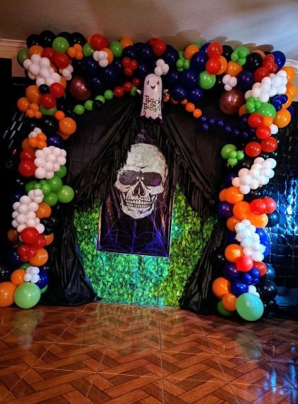 Halloween skull decoration framed by colorful balloon arch and black drapes on a tiled floor