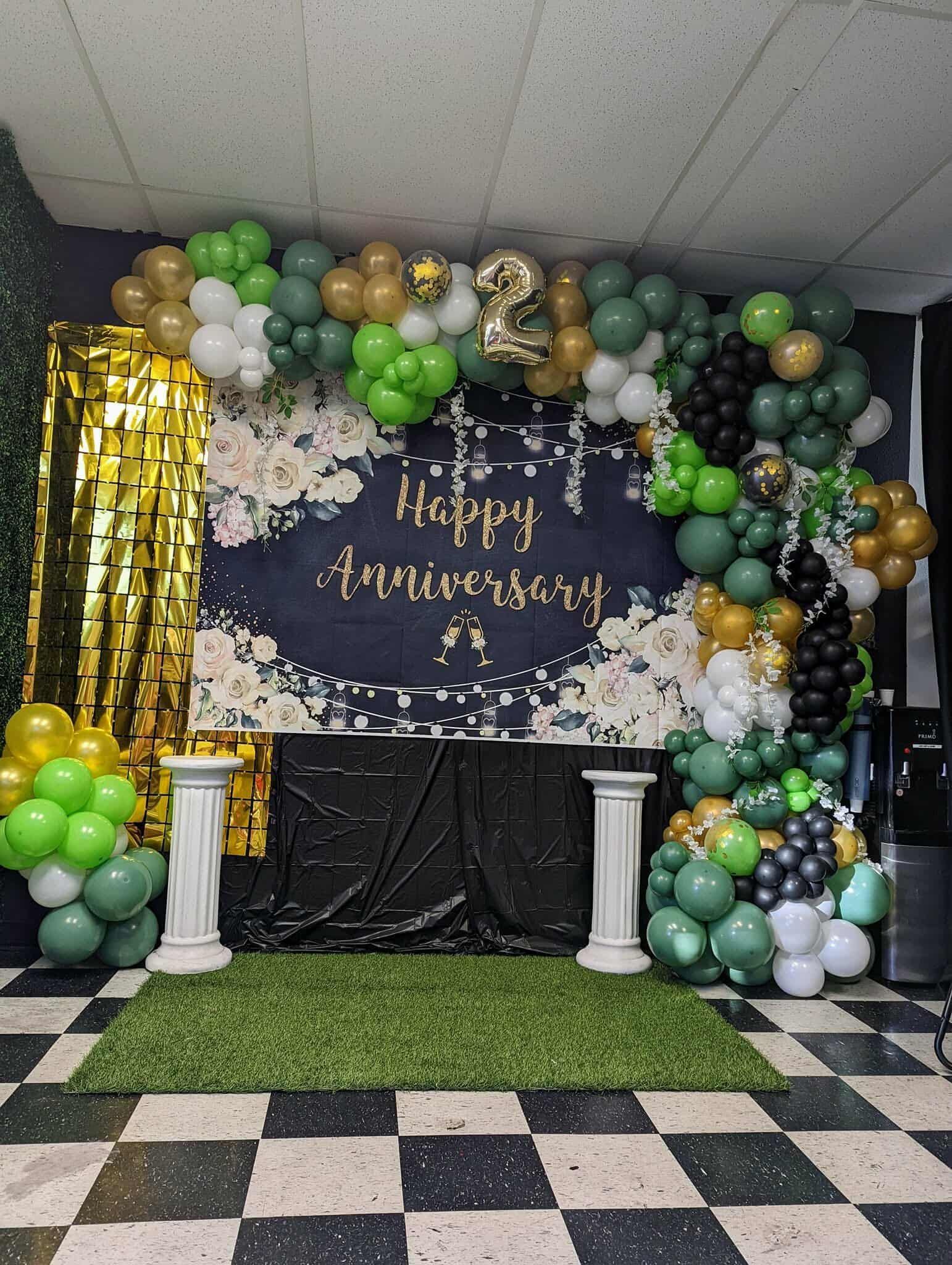 Birthday backdrop with gold, white, and green balloons, black-and-gold decor, and a grass aisle on a checkered floor