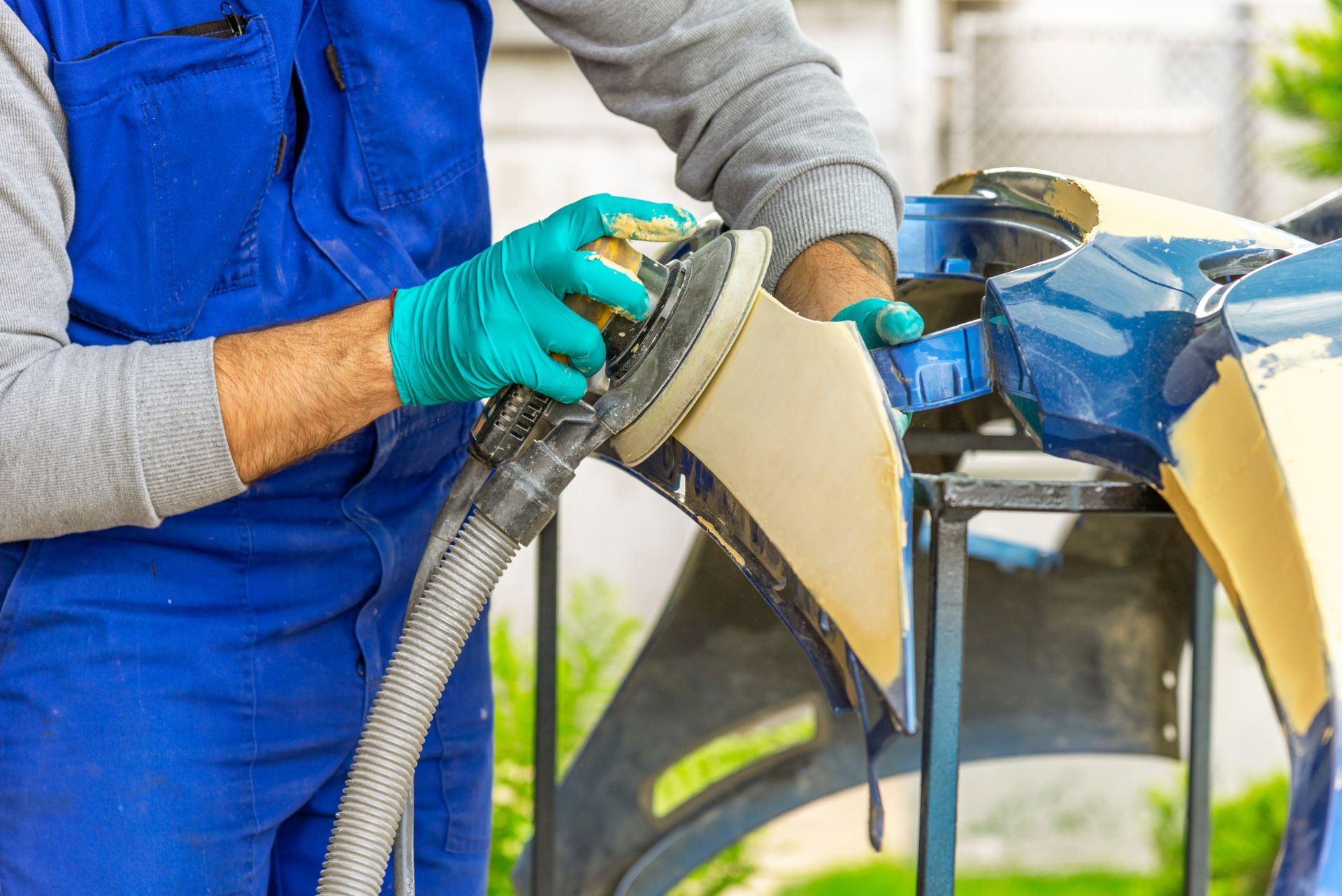 Person in blue overalls using a hose to wash a blue-and-yellow airplane wing