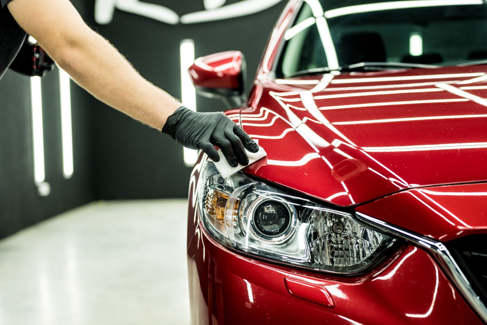 Gloved hand polishing the headlight of a red car in a garage detailing bay