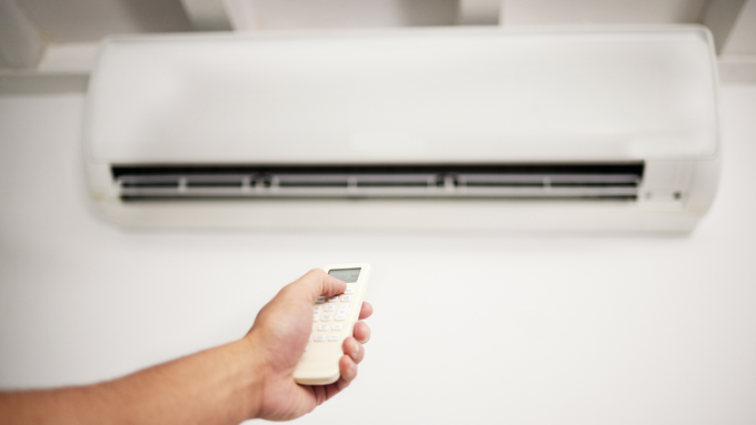 A person is holding a remote control in front of an air conditioner.