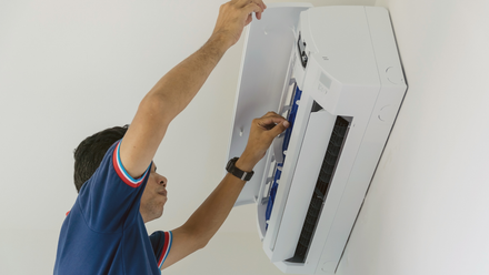 A man is installing an air conditioner on a wall.