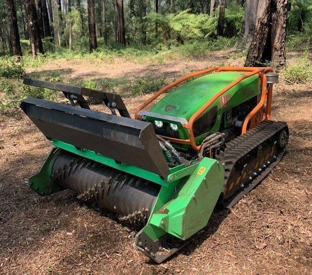Green tracked forestry mulcher with front blade in a wooded area