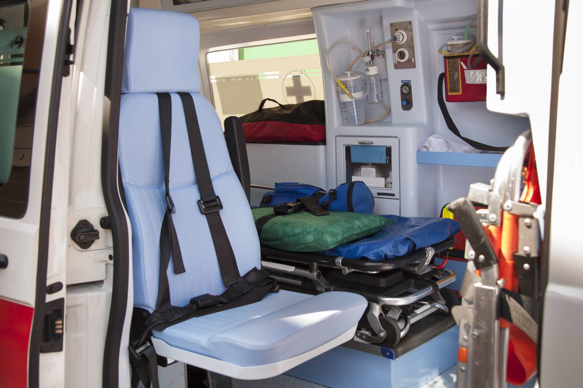 Interno di un'ambulanza con barella, sedile blu e attrezzature mediche visibili.