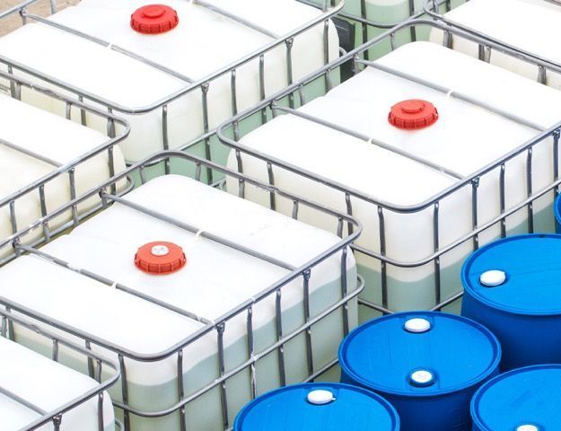 Contenitori per liquidi in plastica bianca e blu con tappi rossi, raggruppati in un'area di stoccaggio.