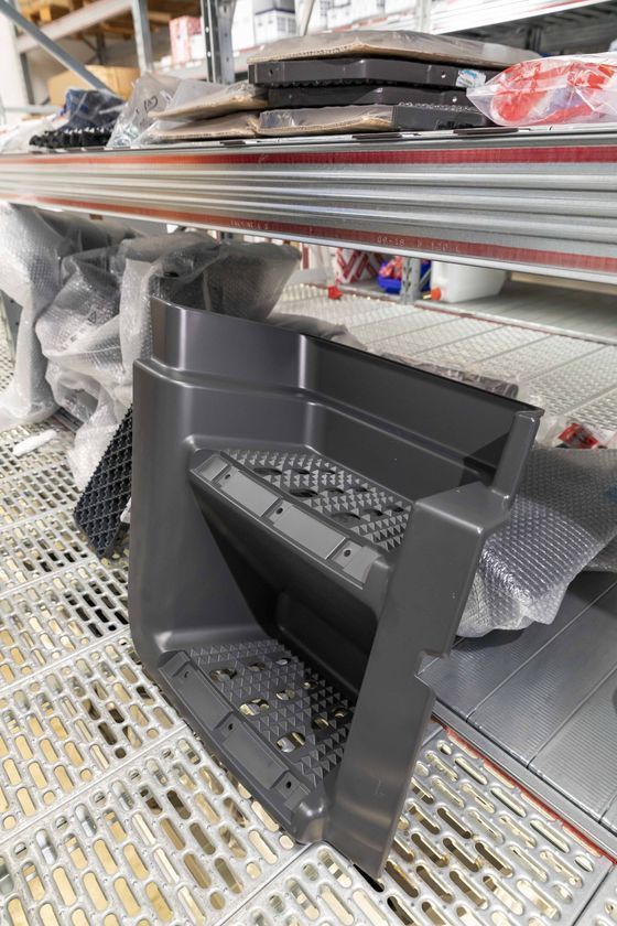 Pannello di rivestimento in plastica nera su uno scaffale di magazzino, avvolto nella schiuma insieme ad altri ricambi auto.