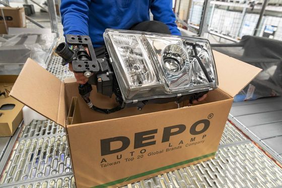 Gruppo faro per auto in una scatola DEPO aperta su un banco da lavoro, con un altro faro accanto.