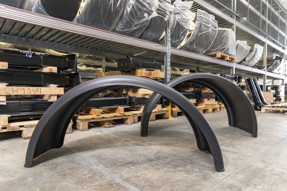 Archi metallici neri e curvi impilati sul pavimento di un magazzino, accanto a pallet e scaffalature.