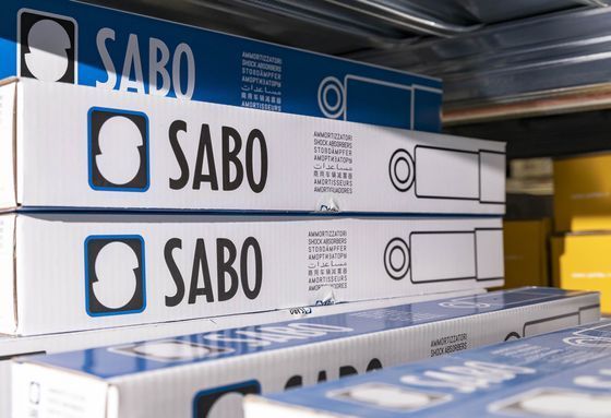 Scatole bianche di SABO impilate sugli scaffali di un negozio, con imballaggi blu sullo sfondo.